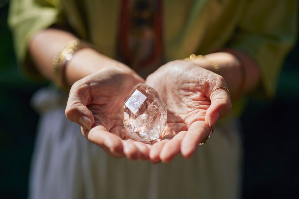 Manos sosteniendo un cuarzo transparente con luz cálida, en un contexto de meditación y trabajo energético consciente 