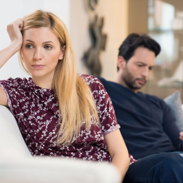 Pareja sentada en el sofá con distancia emocional visible, mirando en direcciones opuestas