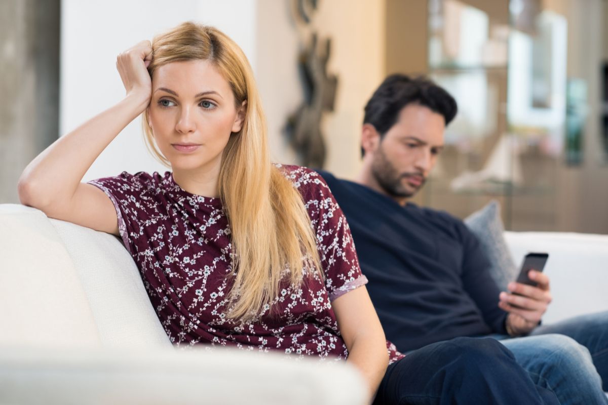 Pareja sentada en el sofá con distancia emocional visible, mirando en direcciones opuestas