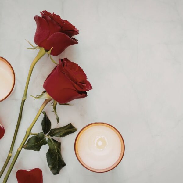 Vela roja encendida junto a pétalos de rosa y elementos de ritual energético sobre una superficie oscura