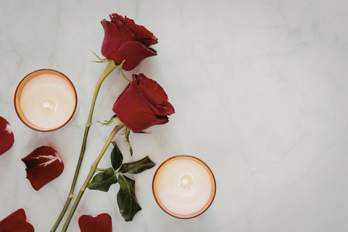 Vela roja encendida junto a pétalos de rosa y elementos de ritual energético sobre una superficie oscura